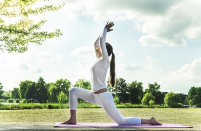 Frau in Yoga-Figur auf Yogamatte auf einer Wiese, Bäume im Hintergrund, Yoga-Beginner